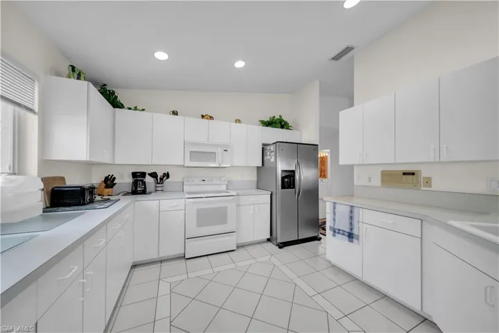 Kitchen featuring white appliances, light countertops, white cabinetry, lofted ceiling, and recessed lighting