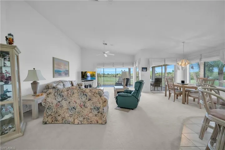 Living area with vaulted ceiling, light colored carpet, hanging lights, and ceiling fan