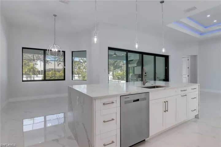 Kitchen featuring white cabinetry, sink, stainless steel dishwasher, decorative light fixtures, and a center island with sink