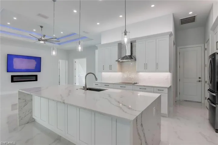 Kitchen featuring a spacious island, wall chimney exhaust hood, and hanging light fixtures