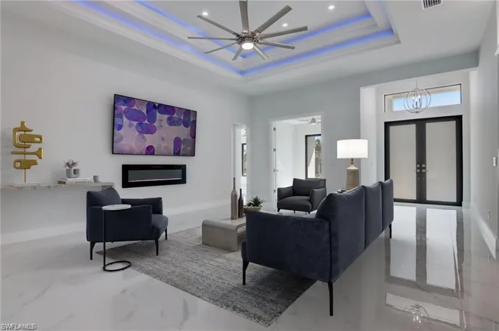 Living room with french doors, ceiling fan with notable chandelier, and a raised ceiling