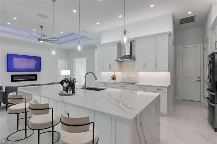 Kitchen with white cabinets, a spacious island, sink, hanging light fixtures, and wall chimney exhaust hood