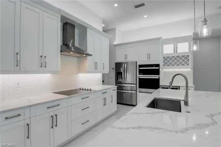 Kitchen with appliances with stainless steel finishes, sink, wall chimney range hood, decorative light fixtures, and white cabinetry
