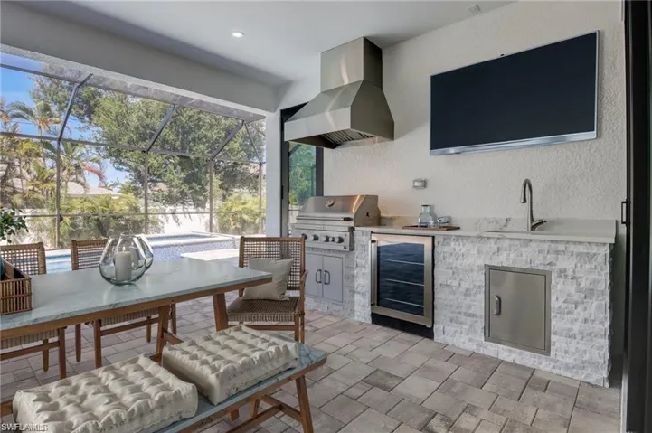 View of patio with sink, an outdoor kitchen, a lanai, wine cooler, and grilling area