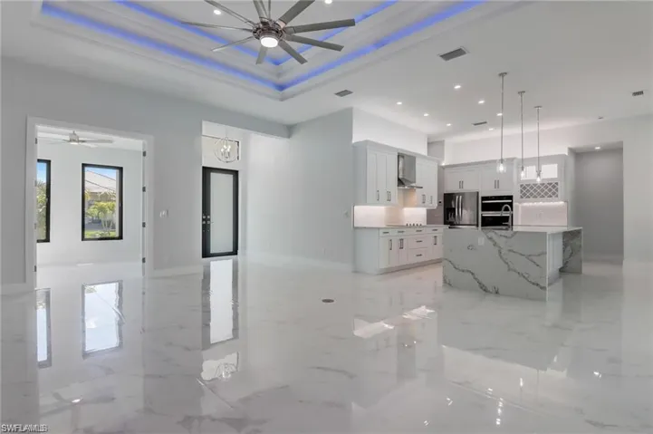 Kitchen featuring a tray ceiling, a spacious island, light stone countertops, and stainless steel appliances
