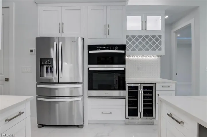 Kitchen with backsplash, wine cooler, white cabinets, and appliances with stainless steel finishes