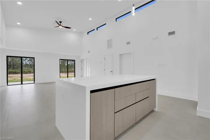 Kitchen featuring light brown cabinets, a towering ceiling, a center island, open floor plan, and concrete floors