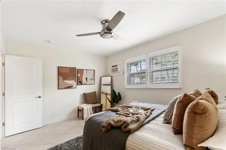 Bedroom featuring light tile patterned flooring, a wall unit AC, and a ceiling fan