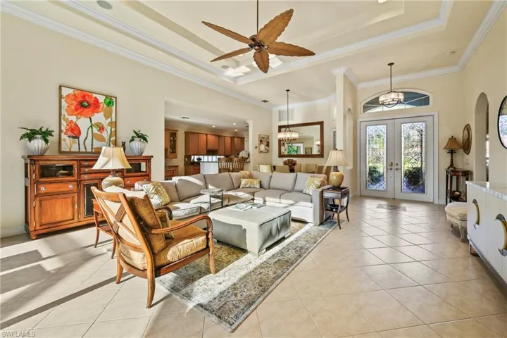 Living room featuring a raised ceiling, light tile patterned floors, a high ceiling, crown molding, and french doors
