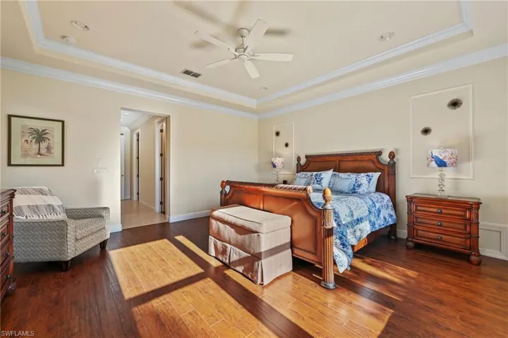 Bedroom featuring a raised ceiling, ornamental molding, dark wood-type flooring, and ceiling fan