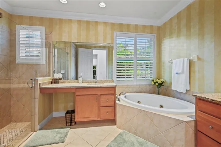 Bathroom with crown molding, healthy amount of natural light, vanity, a whirlpool tub, and wallpapered walls