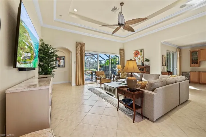Living room featuring a tray ceiling, ornamental molding, light tile patterned floors, a sunroom, and a ceiling fan