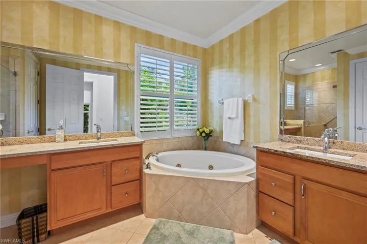 Full bathroom featuring plenty of natural light, wallpapered walls, ornamental molding, two vanities, and a whirlpool tub