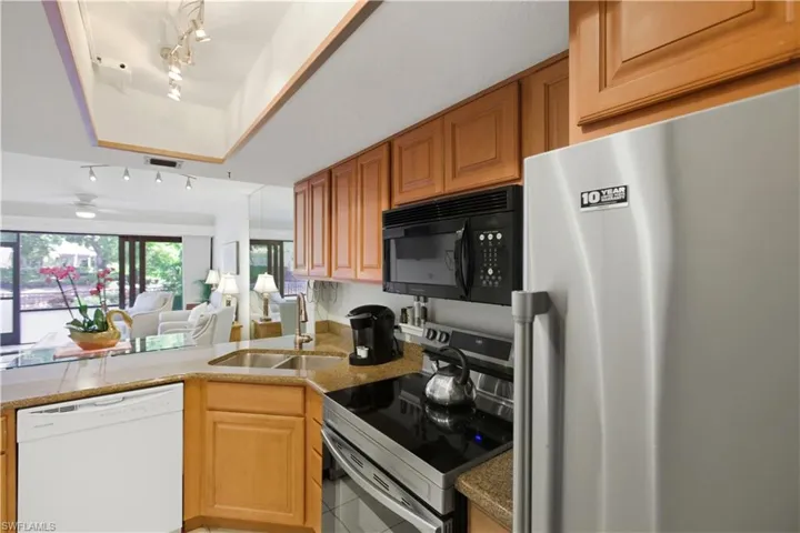 Kitchen featuring stainless steel appliances, track lighting, open floor plan, light stone counters, and light tile patterned flooring