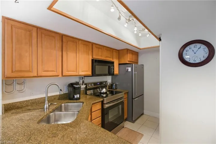 Kitchen with stainless steel range with electric stovetop, black microwave, light tile patterned flooring, brown cabinets, and dark stone countertops