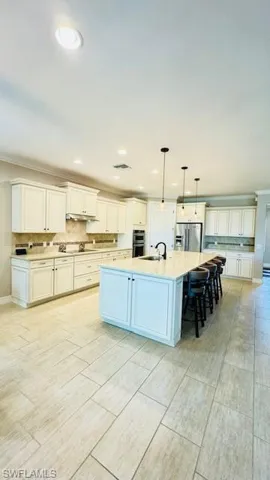 Kitchen featuring white cabinets, pendant lighting, stainless steel appliances, and a center island with sink