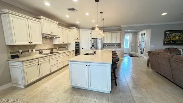 Kitchen featuring sink, an island with sink, stainless steel appliances, and decorative light fixtures