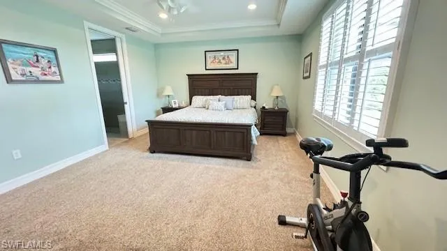Bedroom featuring light carpet, ensuite bathroom, a raised ceiling, and ornamental molding