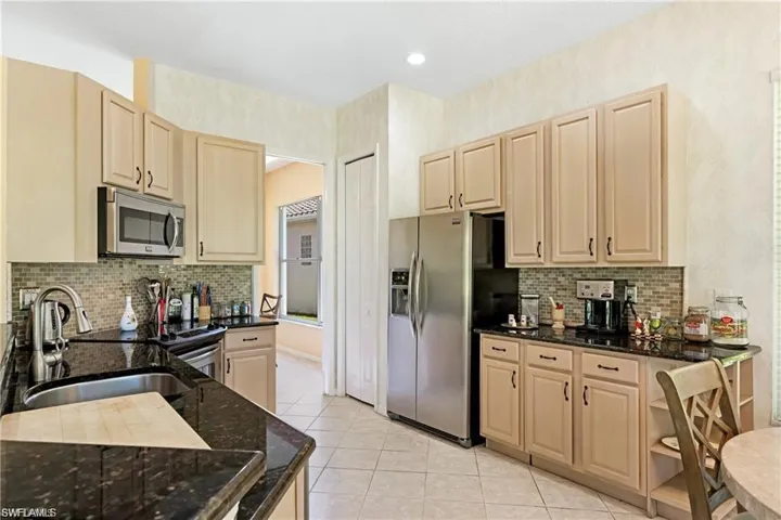 Kitchen with light wood finish cabinets, dark stone countertops, stainless steel appliances, light tile patterned floors, and recessed lighting