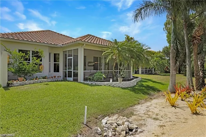 Rear view of property featuring stucco siding, a lawn, a sunroom, and a tile roof