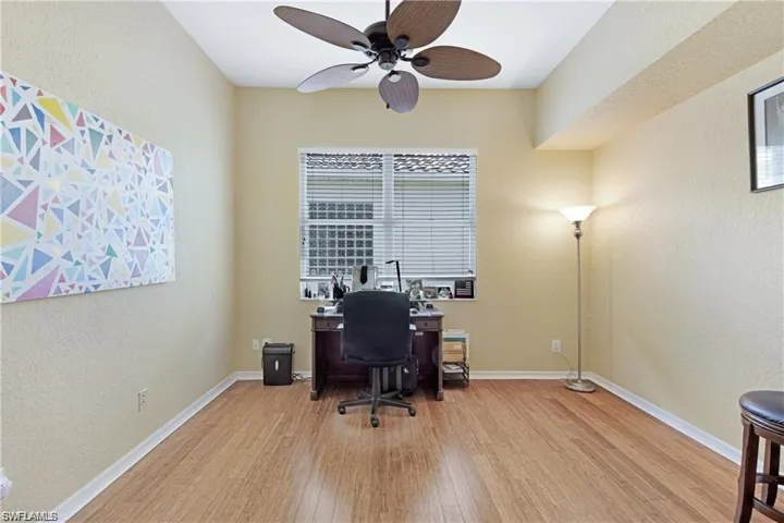 Office with a textured wall, light wood-type flooring, and ceiling fan