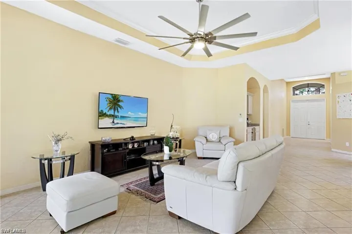 Living room with ornamental molding, arched walkways, a ceiling fan, light tile patterned flooring, and a tray ceiling