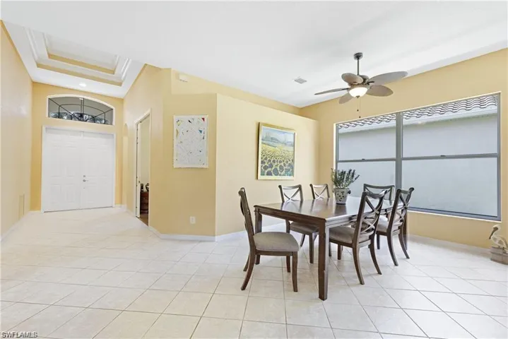 Dining space with ceiling fan, crown molding, light tile patterned floors, healthy amount of natural light, and a raised ceiling