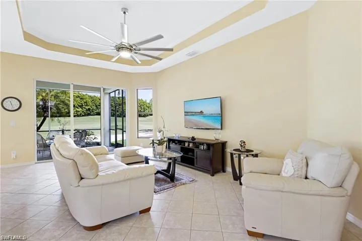 Living room featuring ceiling fan, light tile patterned floors, and a raised ceiling