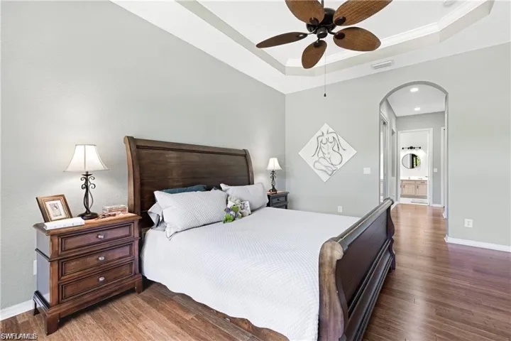 Bedroom featuring arched walkways, wood finished floors, ceiling fan, ornamental molding, and ensuite bathroom