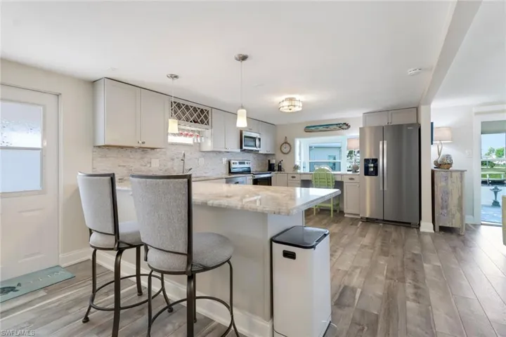 Kitchen with light stone counters, appliances with stainless steel finishes, light hardwood / wood-style flooring, and tasteful backsplash
