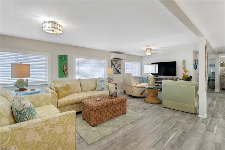 Living room featuring a wall mounted AC, wood-type flooring, and ceiling fan