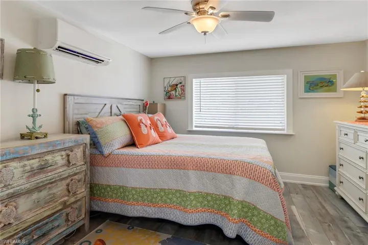 Bedroom featuring a wall mounted AC, hardwood / wood-style floors, and ceiling fan
