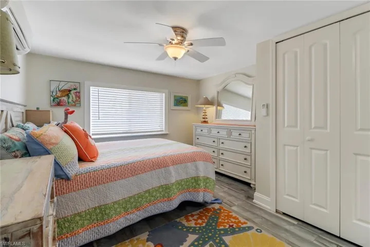 Bedroom with wood-type flooring, a wall unit AC, a closet, and ceiling fan