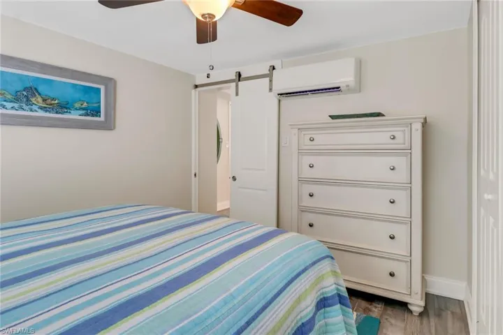 Bedroom featuring a wall mounted AC, dark hardwood / wood-style flooring, a barn door, and ceiling fan
