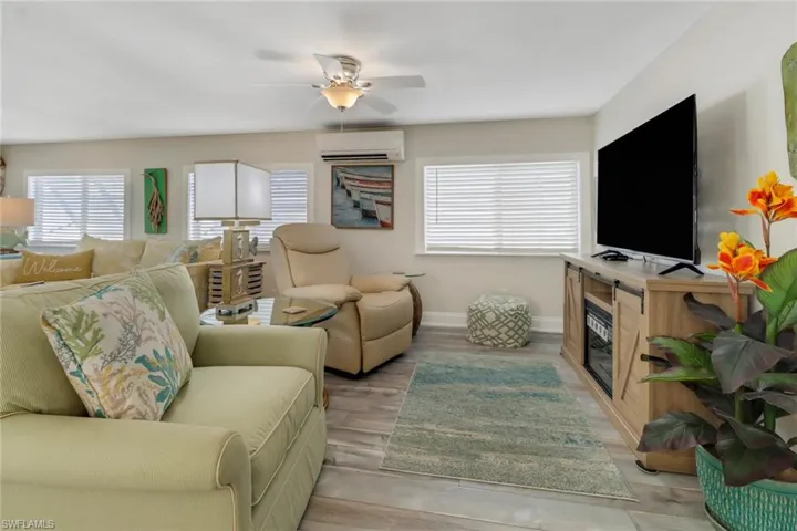 Living room featuring a wall mounted AC, ceiling fan, and light wood-type flooring