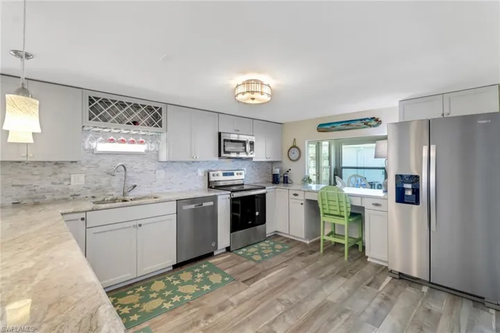 Kitchen with stainless steel appliances, decorative light fixtures, light wood-type flooring, backsplash, and sink