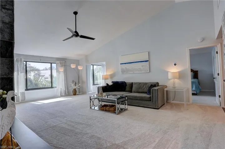 Carpeted living room with ceiling fan and high vaulted ceiling
