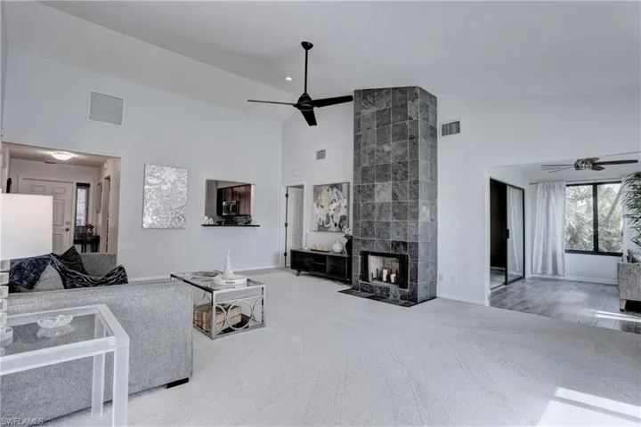 Carpeted living room featuring ceiling fan, high vaulted ceiling, and a fireplace