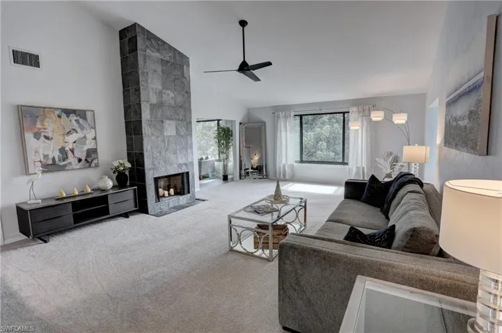 Living room featuring light colored carpet, high vaulted ceiling, a tile fireplace, and ceiling fan