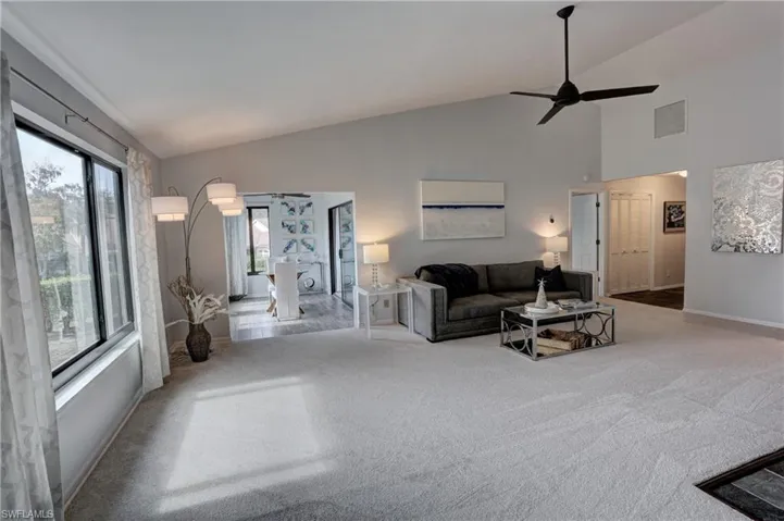 Living room with light colored carpet, high vaulted ceiling, and ceiling fan