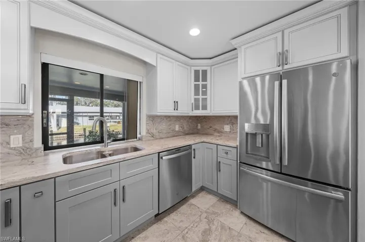 Kitchen with stainless steel appliances, gray cabinetry, light stone countertops, tasteful backsplash, and glass insert cabinets