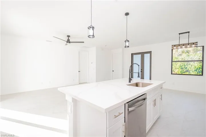 Kitchen featuring open floor plan, white cabinets, dishwasher, pendant lighting, and light stone countertops