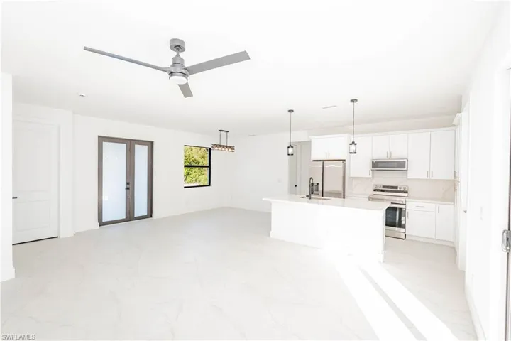 Kitchen with open floor plan, stainless steel appliances, white cabinetry, french doors, and a kitchen island with sink