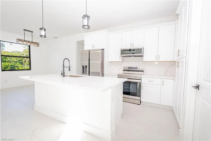 Kitchen with stainless steel appliances, white cabinetry, light marble finish flooring, an island with sink, and hanging light fixtures