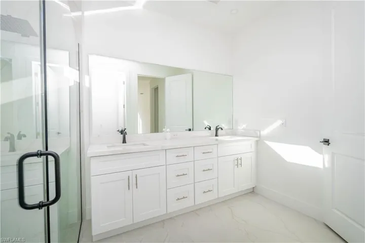 Bathroom featuring a marble finish shower, double vanity, and light marble finish floors