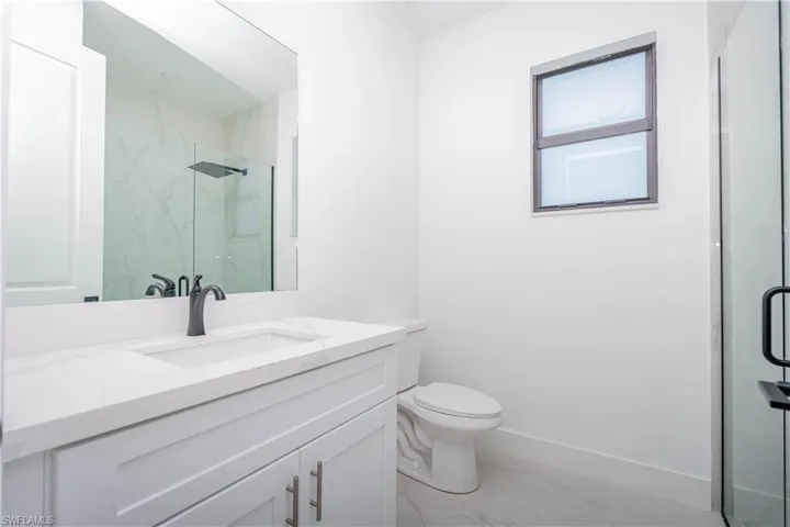 Bathroom featuring vanity, a marble finish shower, and light marble finish flooring