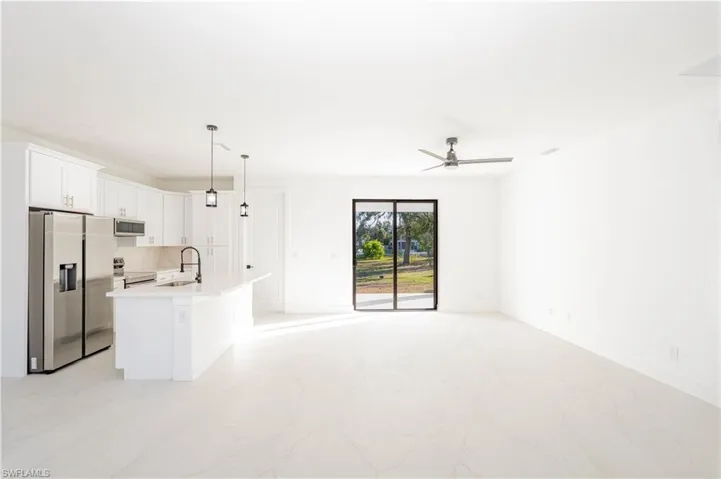 Kitchen featuring stainless steel appliances, open floor plan, white cabinetry, an island with sink, and pendant lighting