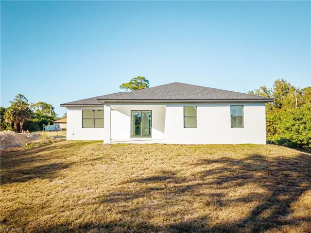 Rear view of property with stucco siding, a lawn, a patio area, and roof with shingles