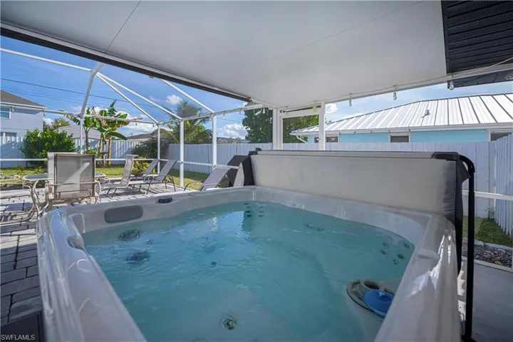 View of swimming pool featuring a hot tub, glass enclosure, a fenced backyard, and a sunroom