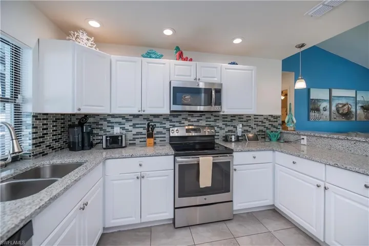 Kitchen featuring stainless steel appliances, white cabinetry, light stone countertops, and hanging light fixtures
